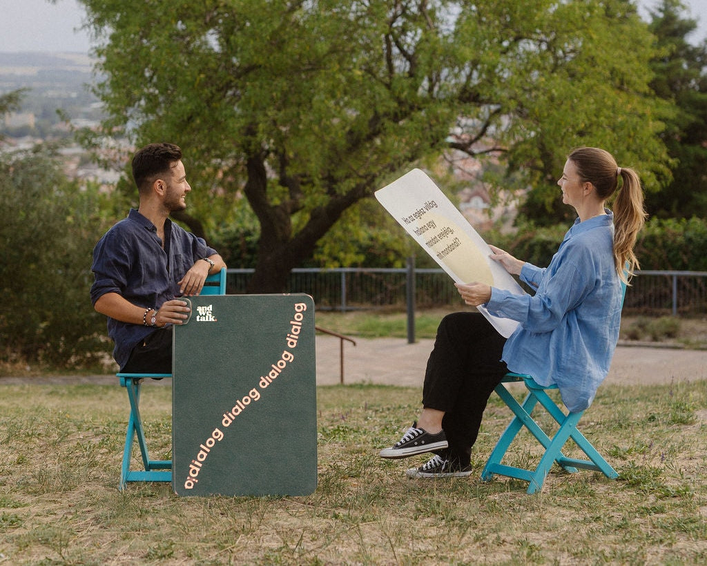 Zwei Menschen unterhalten sich unter Bäumen im Park, mit großen Quality-Time-Karten
